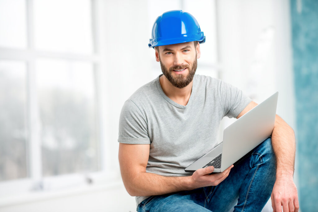 Porträt Bauunternehmer, Vorarbeiters oder Monteurs mit Helm, der mit einem Laptop im weißen Innenraum sitzt. Planungssoftware Digi-Plan 